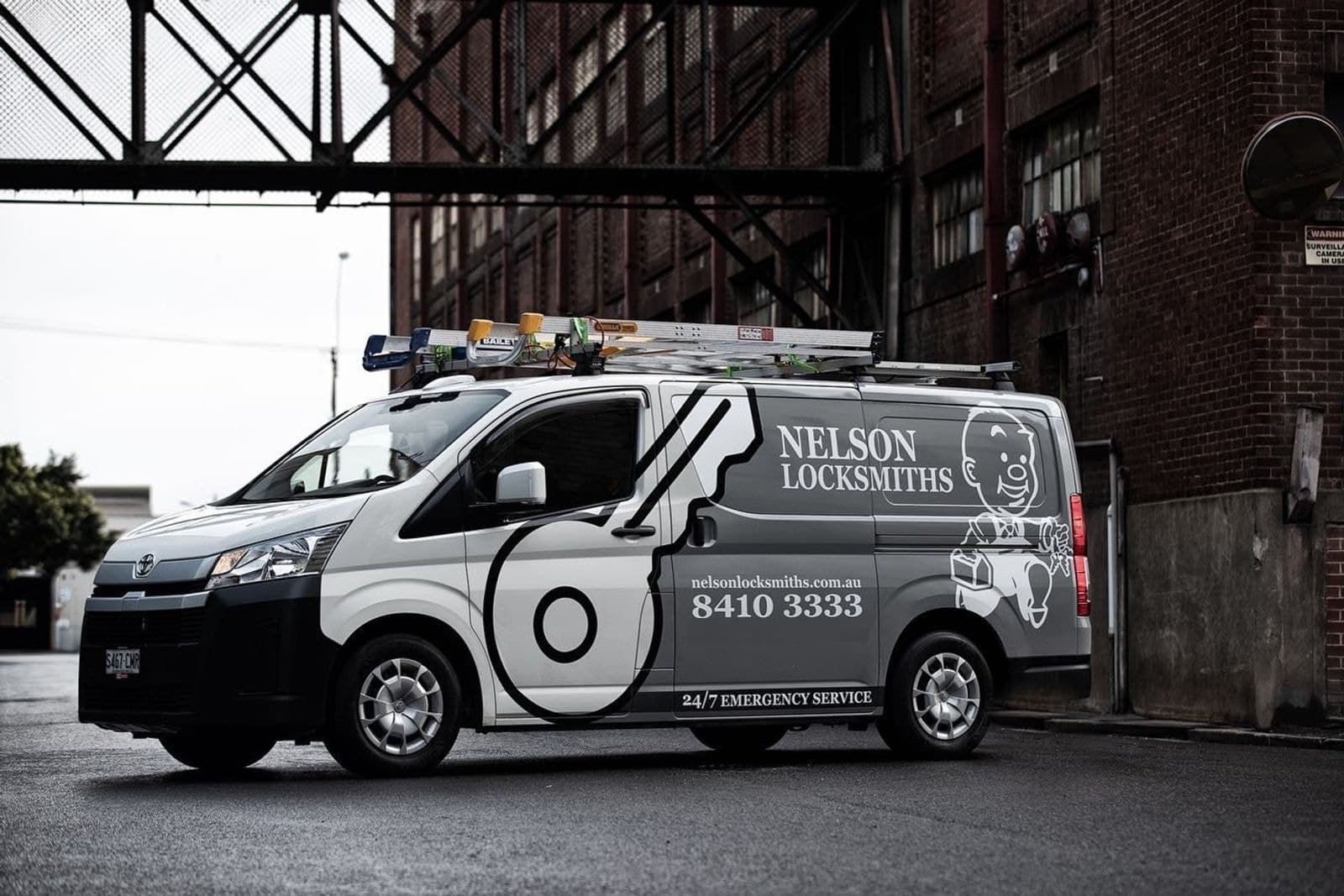 Nelson Locksmiths van parked under a steel walkway beside a brick warehouse